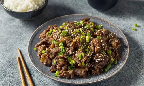 Savory beef bulgogi with scallions and sesame seeds, served beside steamed rice.