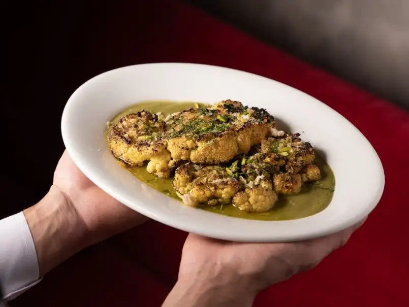 This beautifully plated grilled cauliflower steak is drenched in a flavorful, herby sauce, offering a vegetarian feast for the senses.