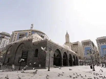 Exterior of Al-Ghamama Mosque, surrounded by pigeons and framed by modern buildings.