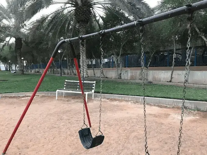 A single swing waiting for play on a quiet evening at a sandy playground.