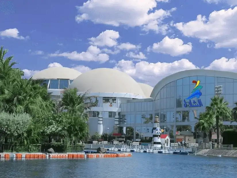 Reflective water body in front of a modern entertainment complex with distinctive domed structures.