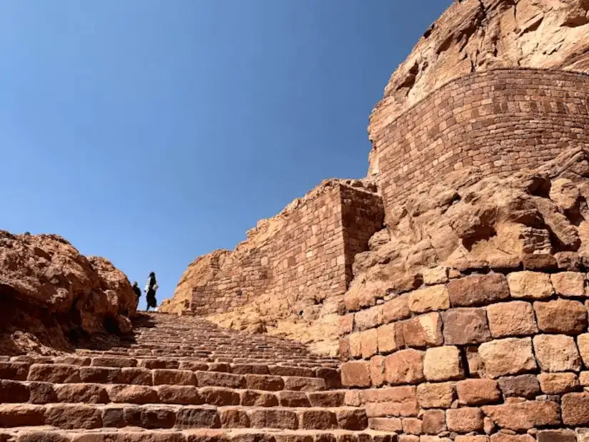 A solitary figure climbs the timeless steps among the rocky terrain.