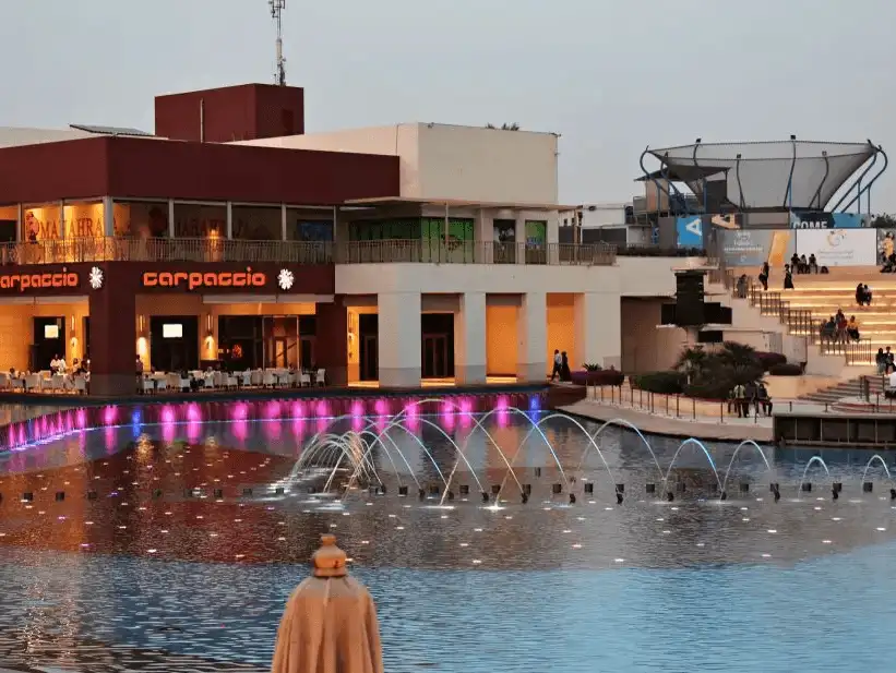 A waterfront dining area illuminated at dusk with vibrant fountain lights, reflecting a lively evening atmosphere.