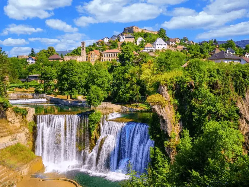 A scenic view of cascading waterfalls with a town backdrop in Bosnia.