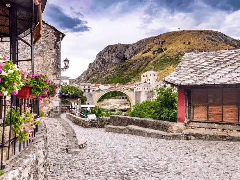 A stone-paved street leading to a historic bridge in a Bosnian town.