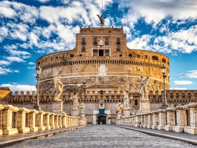 The imposing Castel Sant'Angelo standing proudly under a bright blue sky, with statues lining the bridge.