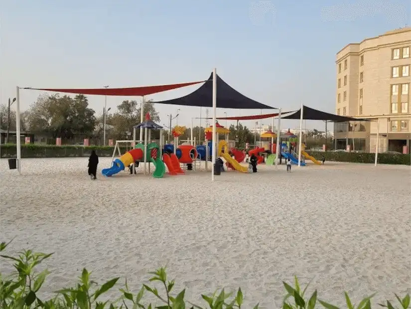 Spacious sand-covered playground with various play structures under partial shade in Dolphin Park.