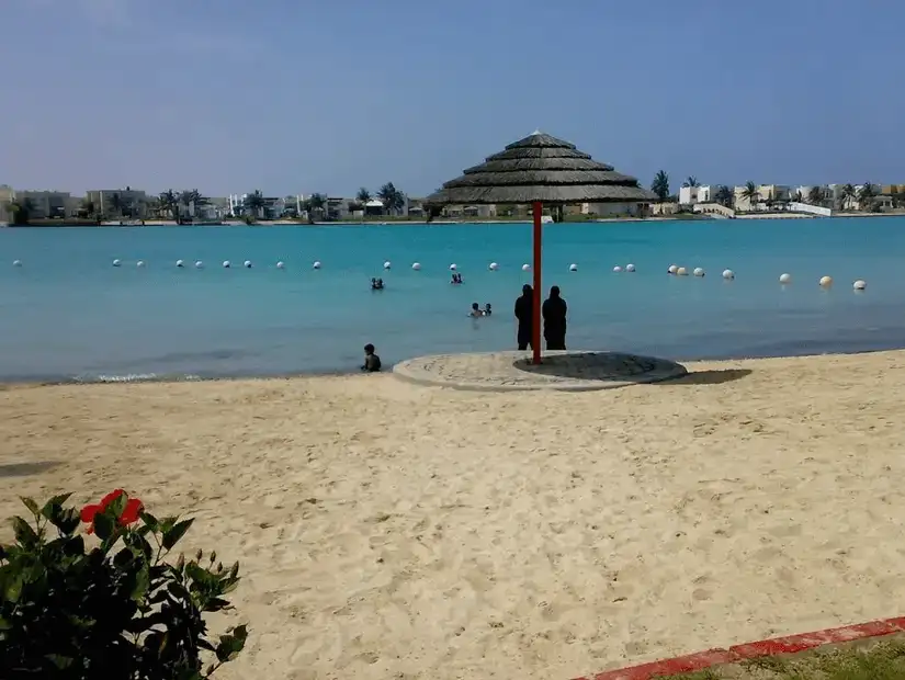 Idyllic beach scene with a thatched-roof shelter and swimmers enjoying the clear shallow waters.