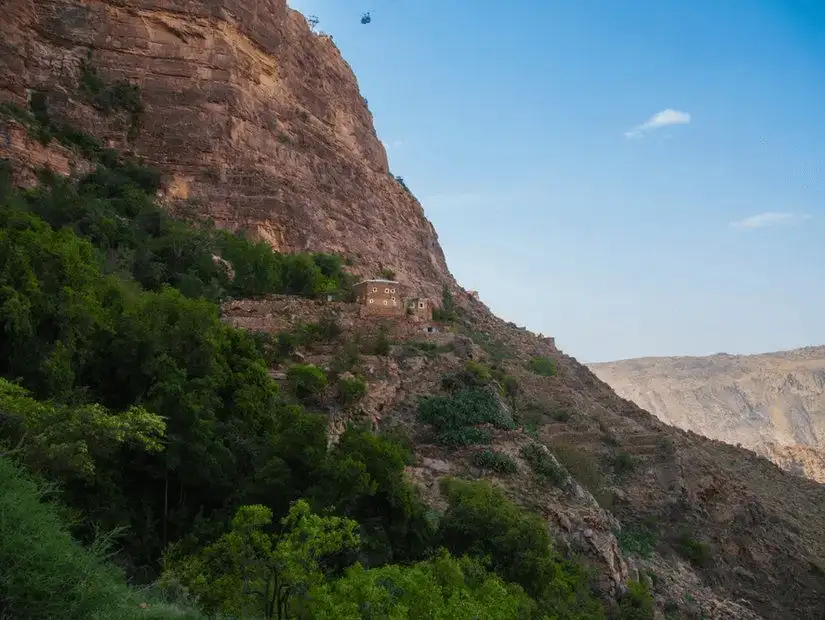 A house perched on a steep mountainside, nestled among lush greenery, showcasing nature's harmony with human habitation.