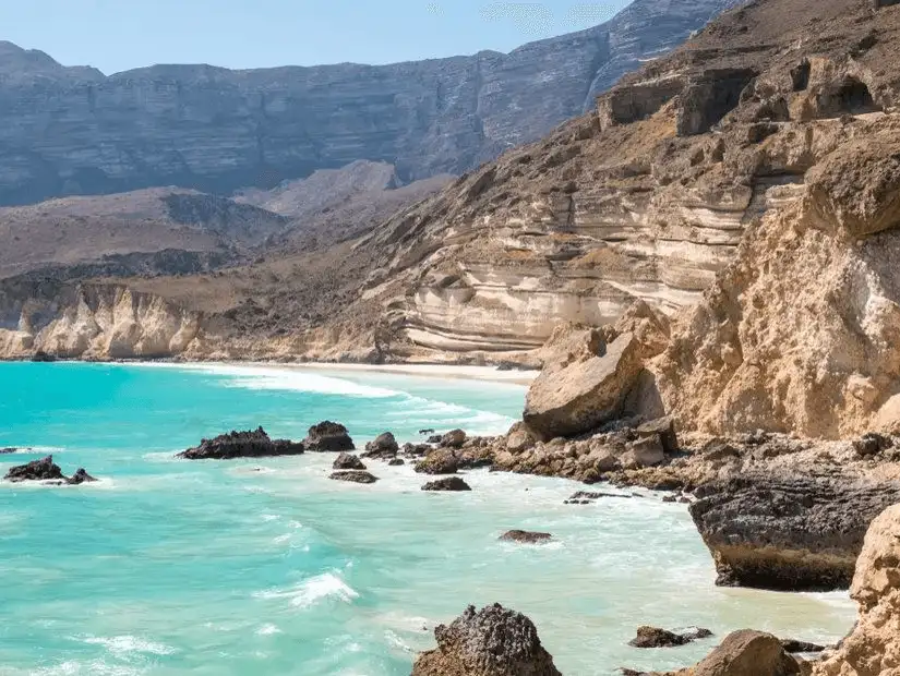 The stunning blue waters and cliffs of Fazayah Beach under a clear sky.