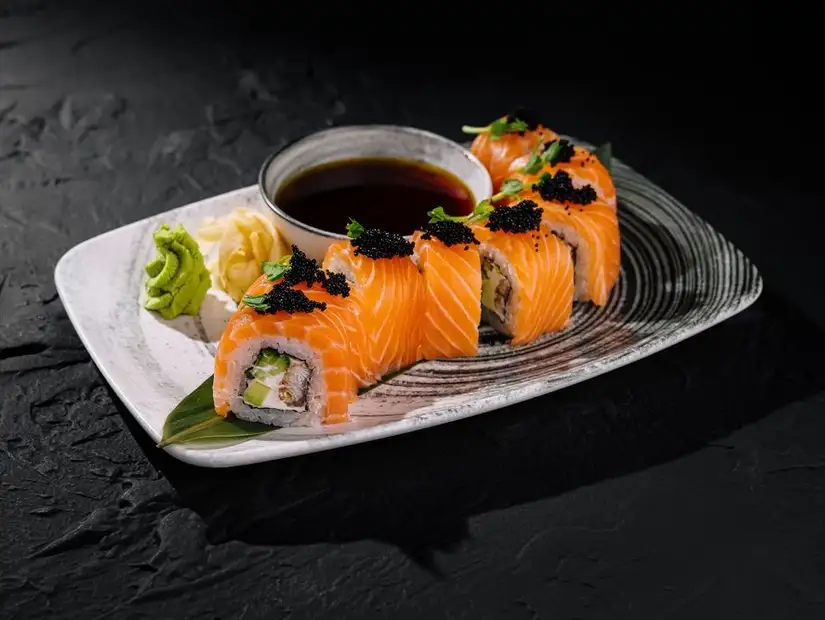 Hand presenting a plate of fresh salmon sushi rolls.