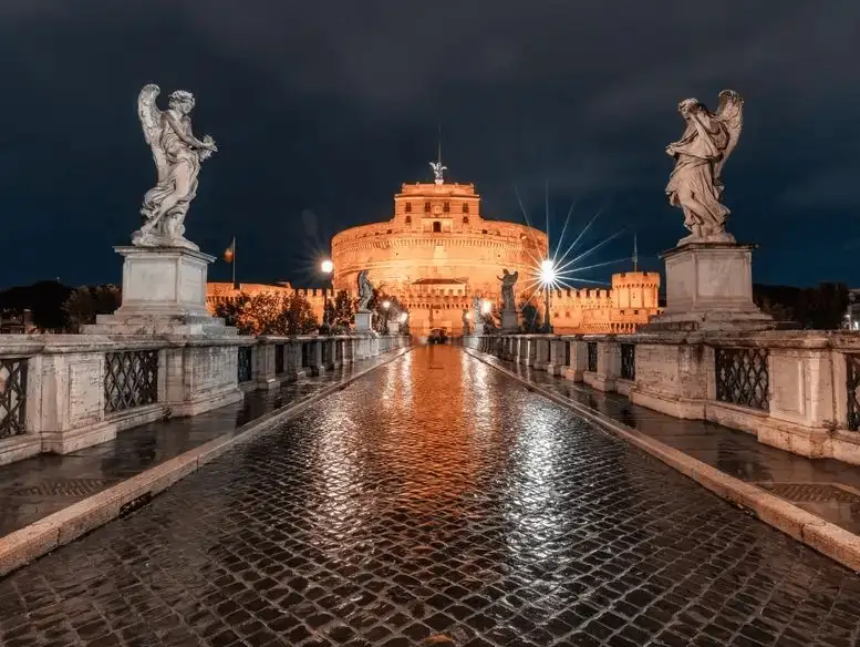 The majestic Castel Sant'Angelo illuminated against the night sky, with statues guarding the entrance.