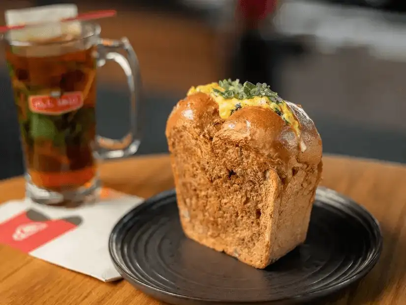 A freshly baked loaf of bread served on a black plate with a glass of mint tea in the background.