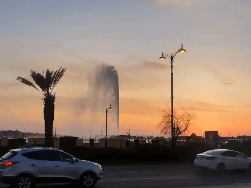 A cityscape at sunset with a towering water fountain.