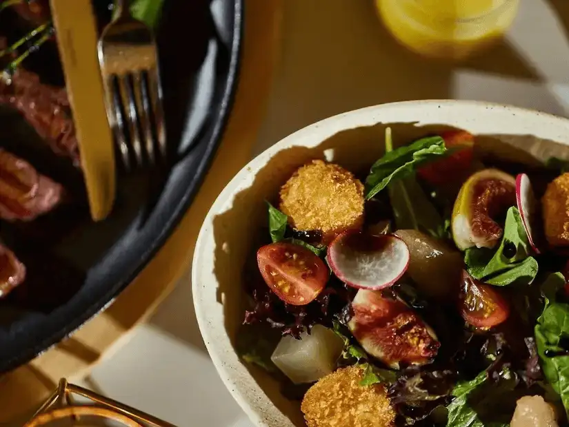 A sophisticated salad with crispy golden croquettes, sliced figs, and cherry tomatoes, highlighting fresh, vibrant flavors.