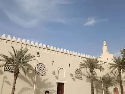 The historic Miqat Mosque, framed by palm trees and a clear sky.