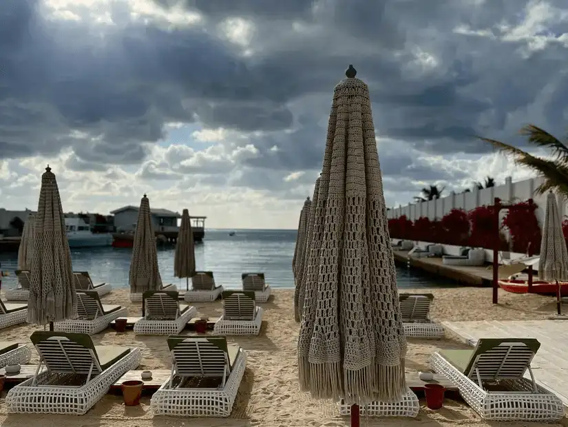 Deserted beach loungers under closed umbrellas on a cloudy day, with a hint of an approaching storm.