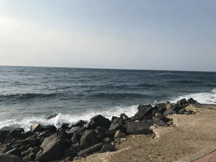 Rocky shoreline with waves crashing against boulders under a clear sky.