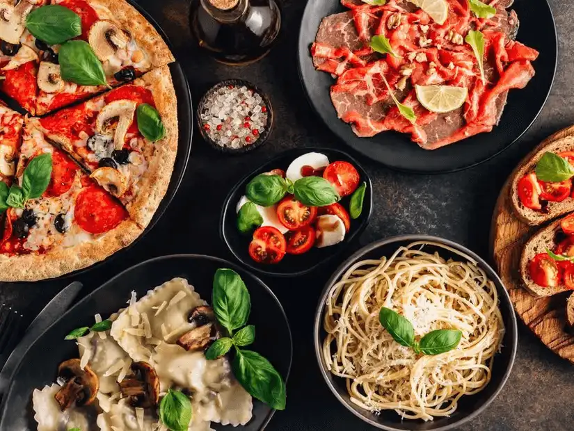 An Italian feast with pizza, ravioli, spaghetti, and a selection of fresh salads and meats.