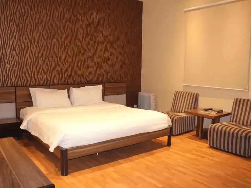 A neat and inviting hotel room with a large bed, striped chairs, and a minimalist design.