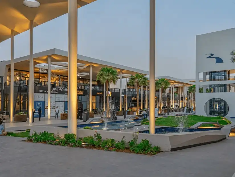 The elegant entrance of Riverwalk Dining & Shopping Center in the evening, accentuated by fountains and palm trees.