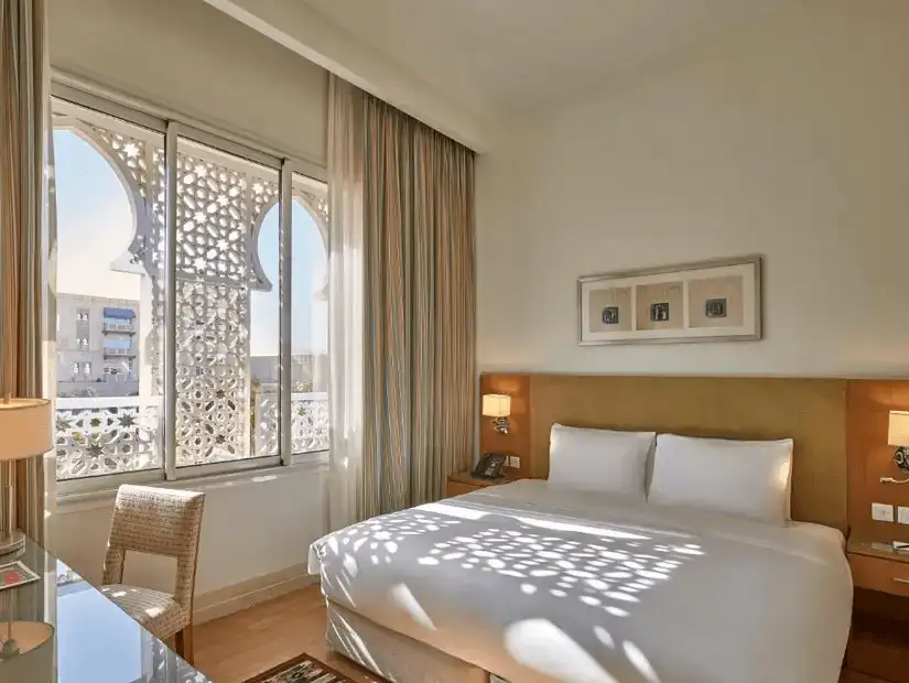 Light filters through an intricately designed window in a bright room at Salalah Gardens Hotel.