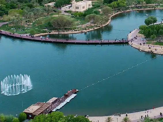 Overview of a park lake with a fountain and surrounding walkways filled with visitors.