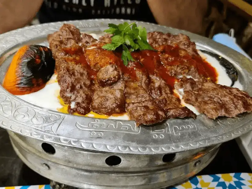 Grilled meat served over a bed of yogurt and tomato sauce, with a side of roasted vegetables.