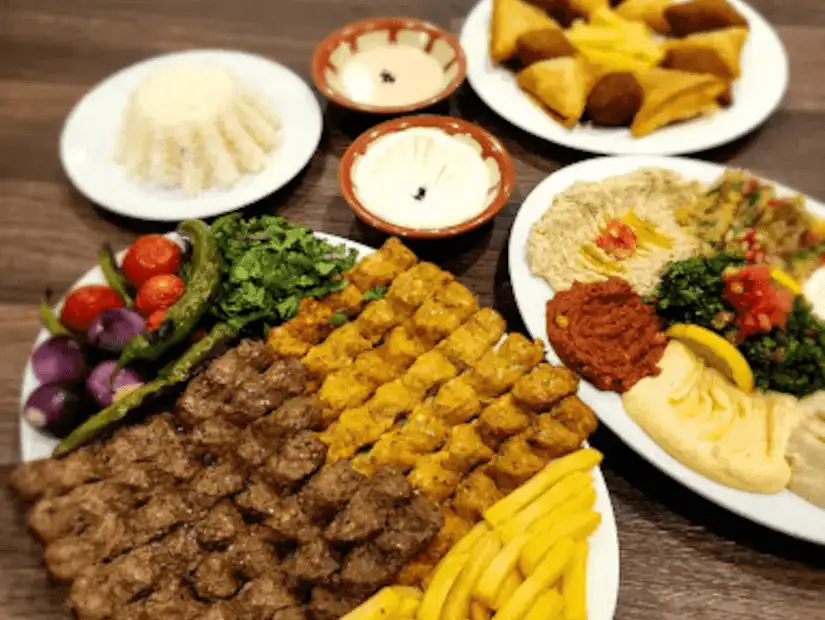 Middle Eastern grill with an array of kebabs, hummus, and sides on a wooden platter.