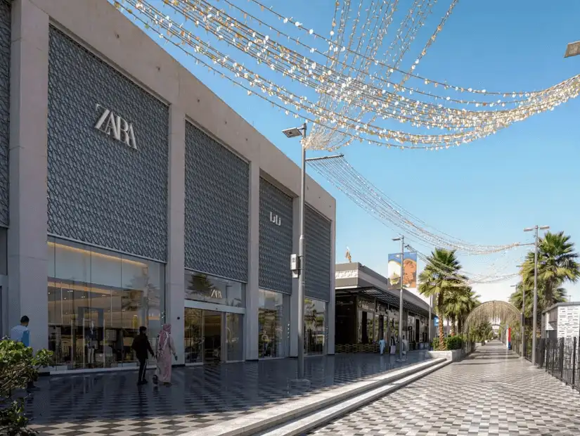 A serene, palm-lined promenade in front of fashionable retail stores under a bright blue sky.