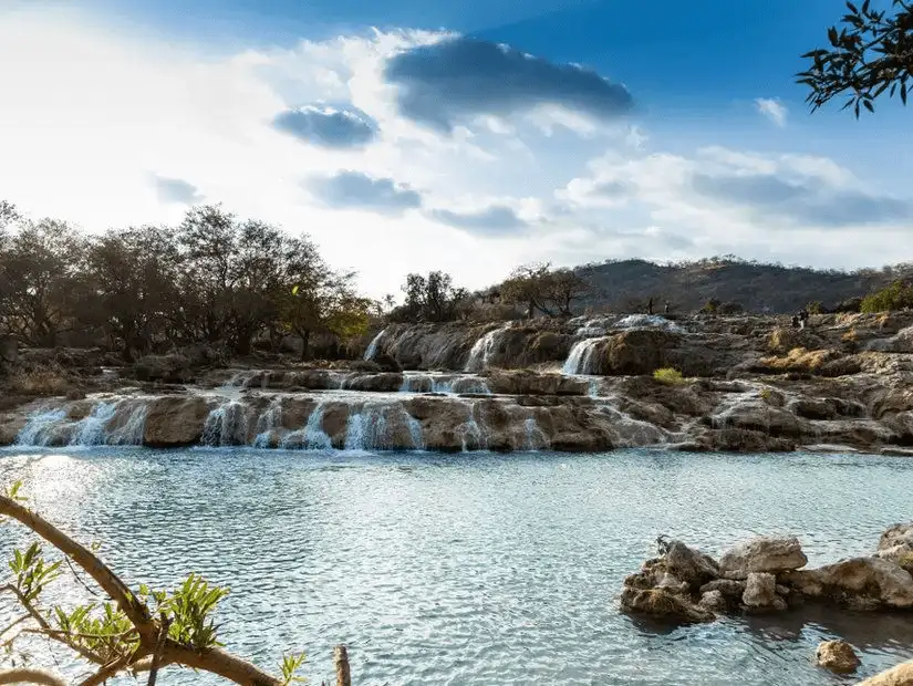 Tranquil waters cascade over terraced rocks at Wadi Darbat, a picturesque oasis.