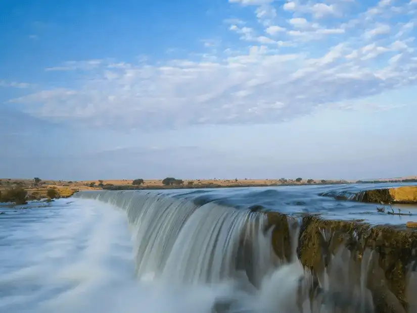 The powerful flow of water cascades over the falls under a sky streaked with clouds.