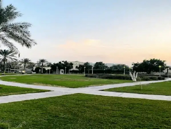 A serene view of Abdullah Al-Salem Park at sunset, surrounded by palm trees and green lawns.