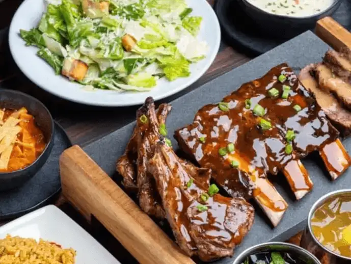 Platter of BBQ ribs and sides served with a glossy barbecue sauce.