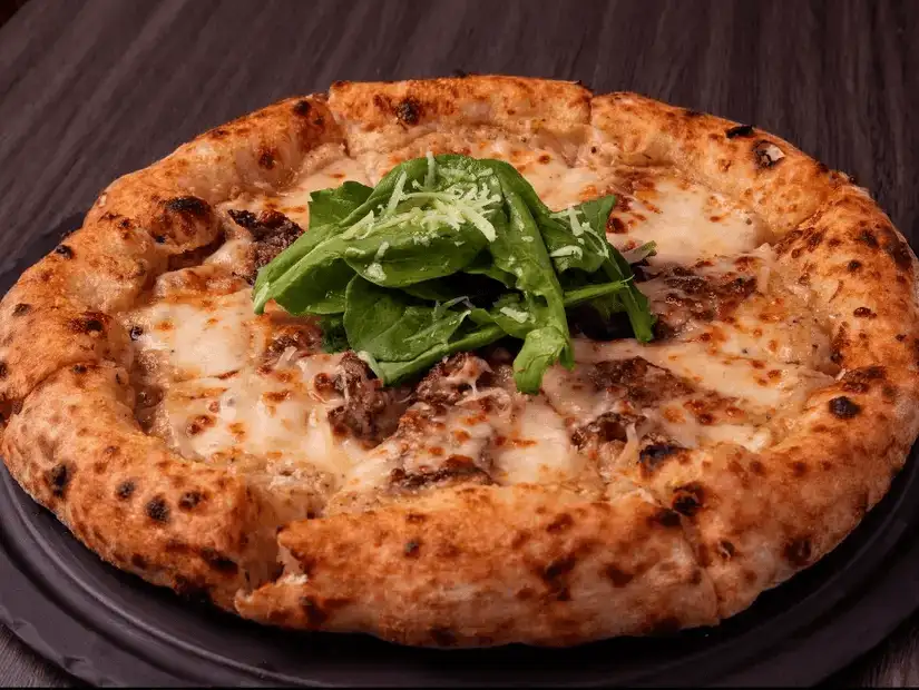 Wood-fired pizza topped with sausage and fresh arugula on a blistered crust.