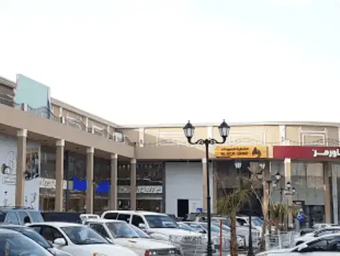 Open-air shopping complex with multiple stores and parked cars.