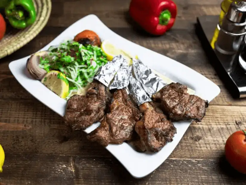 Grilled lamb chops served with lemon and a side of onions, accompanied by charred tomatoes and green peppers.