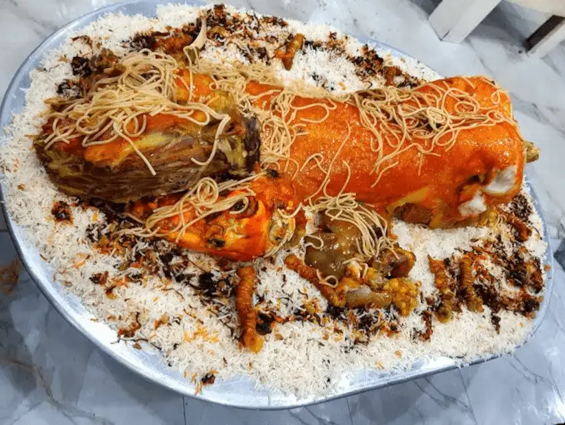 A large platter of mixed rice with lamb shank, topped with fried onions and almonds, a traditional Gulf region feast.