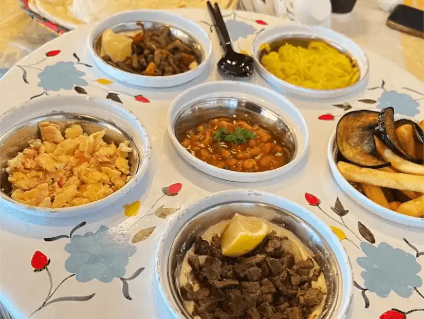 A lavish Saudi breakfast spread featuring falafel, sautéed eggplant, scrambled eggs, and traditional tea.