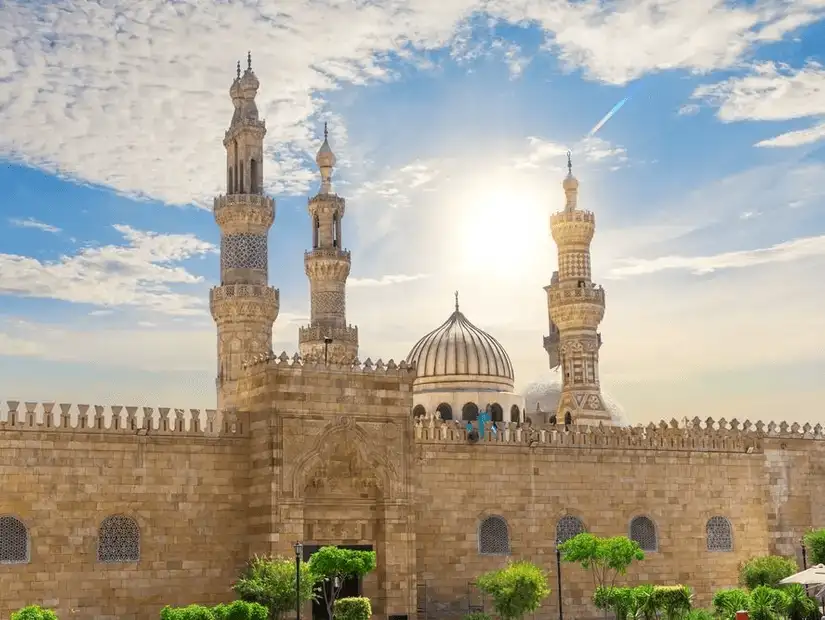 A stunning view of the Al-Azhar Mosque, bathed in sunlight with intricate minarets against a blue sky.