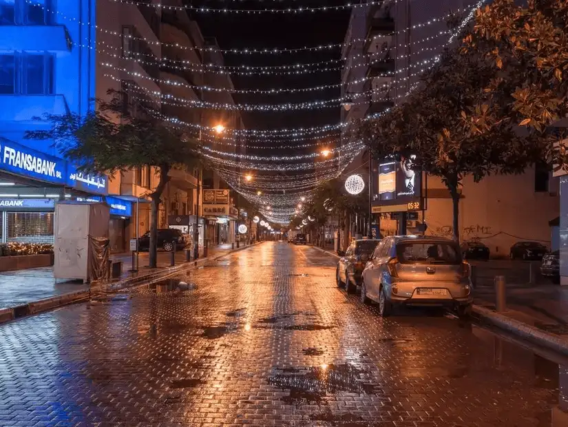 Al Hamra Street lit up at night, with festive lights reflecting off the wet pavement, creating a lively atmosphere.