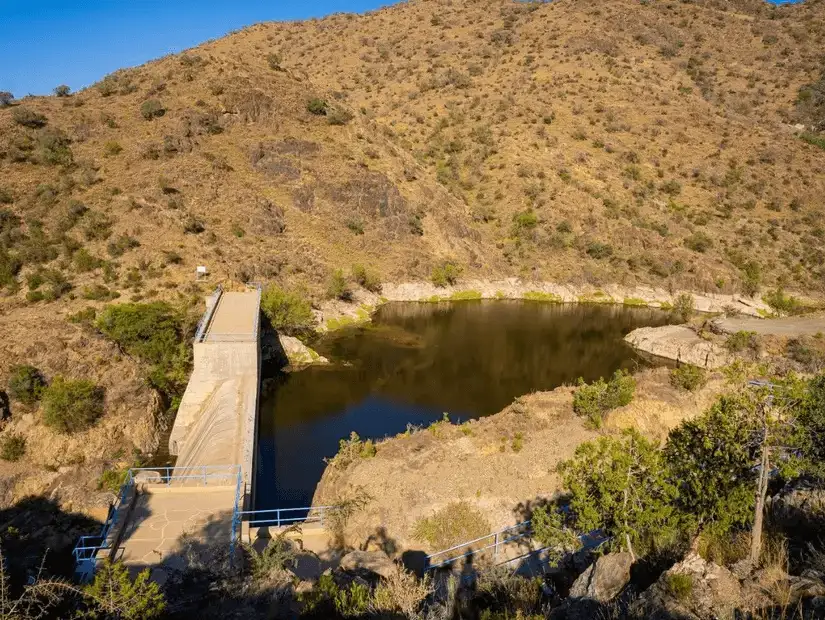 Serene reservoir nestled in the hills of Al-Khaira Forest.