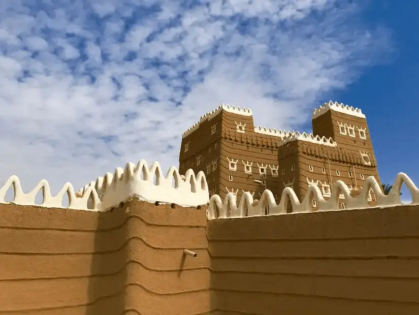 The imposing Al Manjam Palace, a traditional mud-brick fortress with ornate white crenellations.