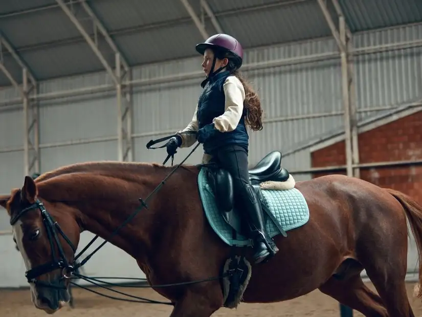 Young girl riding a horse in an indoor equestrian facility.