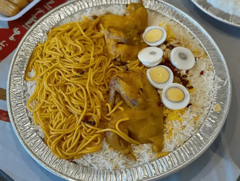 A vibrant dish of rice, chicken, and noodles, served with boiled eggs and spices.