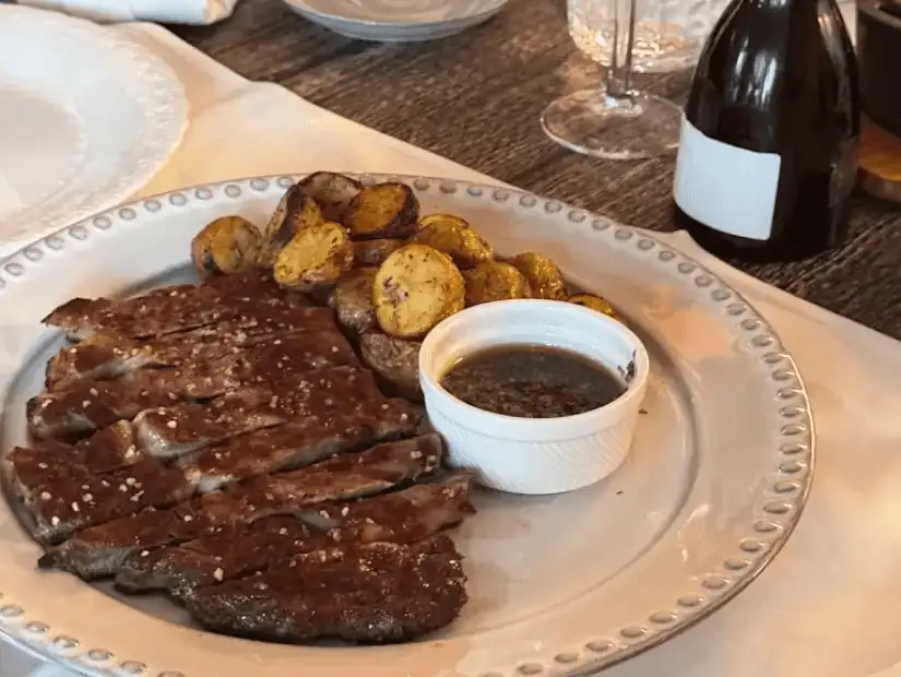 A mouth-watering dish of grilled meat, served with roasted potatoes and a side of green sauce for extra flavor.