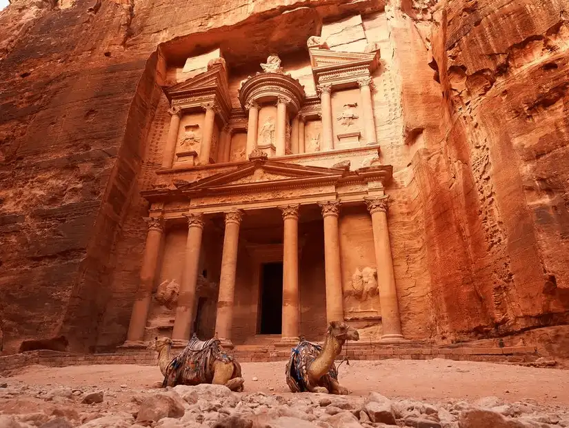 Camels rest by the iconic ancient façade carved into rose-red cliffs.