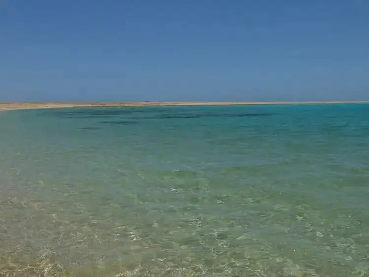 Serene sea view at Atawil, featuring shallow azure waters and a distant sandy spit under clear skies.