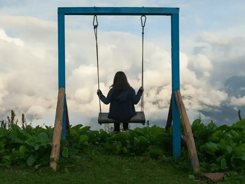 A person sitting on a swing overlooking a stunning mountainous landscape.