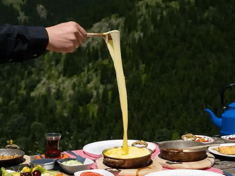 A person pulling melted cheese from a plate of traditional food in a mountainous setting.
